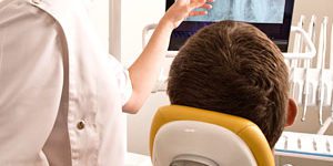 Woman dentist showing to patient on dental chair result of his dental x-rays on screen