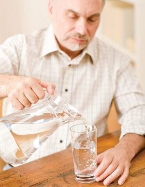 Elderly man pouring water in drinking glass to prevent dry mouth