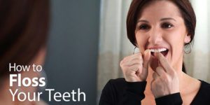 Woman Flossing Teeth in front of a mirror