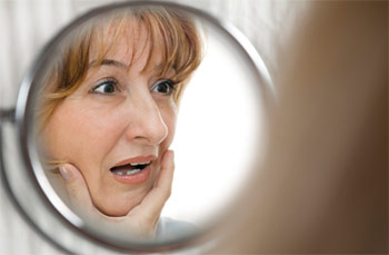 Woman looking surprised in the mirror due to missing teeth