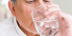 Elderly man drinking a glass of water to prevent chronic dry mouth