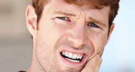 Man touching left cheek due combined root canal and gum problems