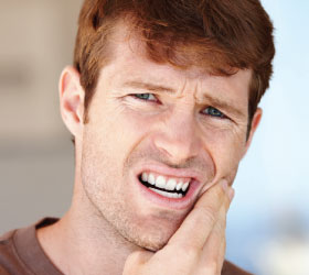 Man touching left cheek due combined root canal and gum problems